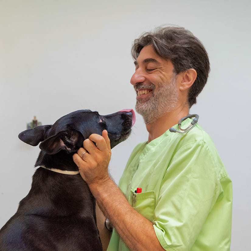 dottore sorridente che guarda il cane nero davanti a lui mentre lo accarezza
